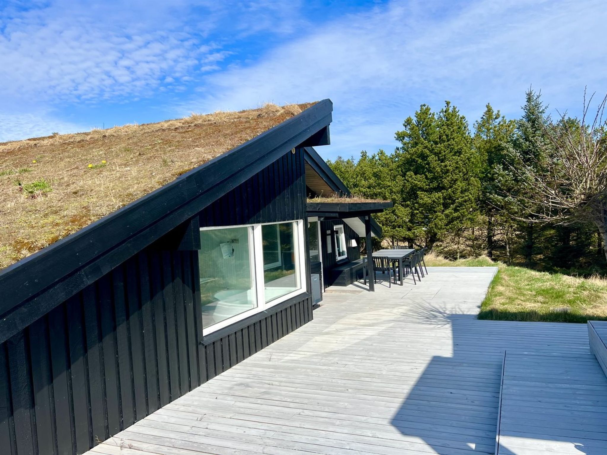 Una casa moderna con techo inclinado, ventanas grandes y una terraza de madera.