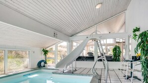 Una piscina interior con tobogán, zona de estar y plantas en macetas.