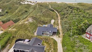 Une propriété située sur la côte, comprenant une maison principale et une dépendance plus petite, le tout entouré de dunes et de végétation.