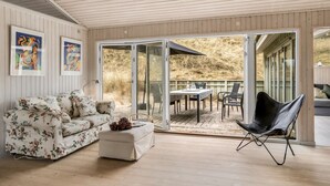 Un intérieur moderne avec un plafond en bois, un canapé à motifs floraux, une chaise pliante noire et une porte-fenêtre coulissante donnant sur un patio extérieur.