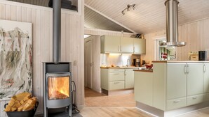 Une cuisine moderne dotée d’un poêle à bois, de meubles de couleur claire et d’un îlot central bien visible, équipé d’un évier.