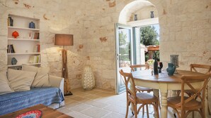 A cozy room with a sofa, a table, and chairs, a bookshelf, and a view through an open door. - TD Trulli Della Magnolia Trulli w Amazing Garden (Monopoli)