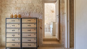 A stone wall, wooden storage units, and a doorway leading to a room with a bed and a nightstand. - TD Trulli Della Magnolia Trulli w Amazing Garden (Monopoli)