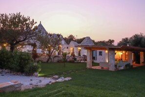 A stone building with a conical roof, a covered outdoor seating area, and a well-maintained garden. - TD Trulli Della Magnolia Trulli w Amazing Garden (Monopoli)