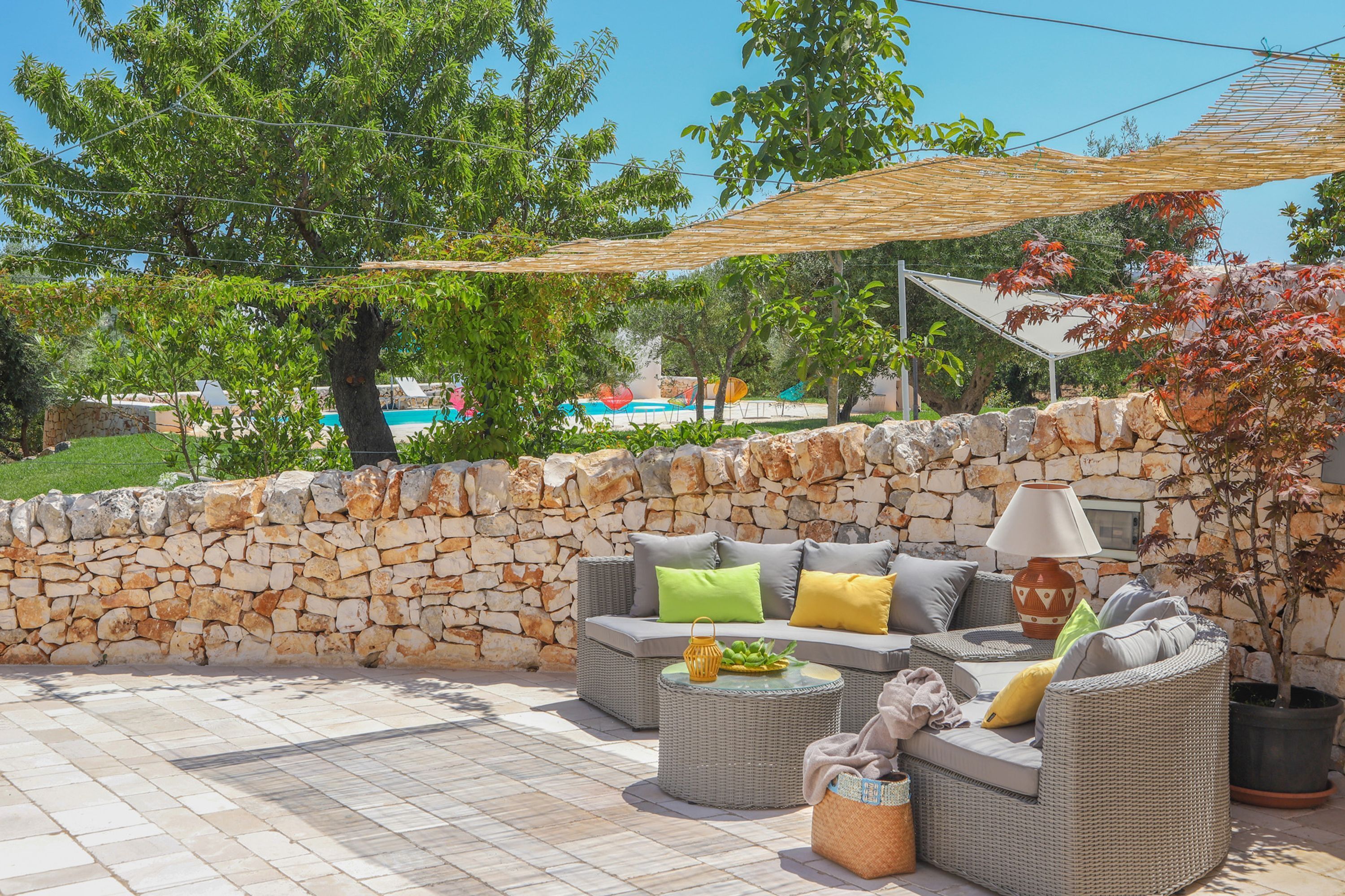 An outdoor seating area with wicker furniture, a stone wall, and a potted plant.