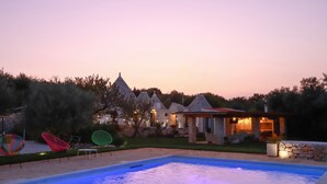 A swimming pool with a stone structure in the background, surrounded by colorful chairs and a small building. - TD Trulli Della Magnolia Trulli w Amazing Garden (Monopoli)
