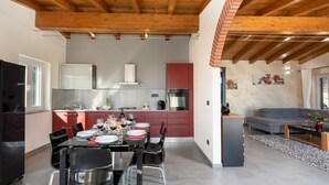 A modern kitchen with red cabinets, a dining area with a table set for four, and a grey sofa in the living room. - Villa Vittorio 6 2 Emma Villas (Imperia)