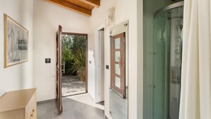 A hallway with a wooden door leading to a garden, a glass shower enclosure, and a framed picture on the wall. - Villa Vittorio 6 2 Emma Villas (Imperia)
