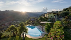 Una piscina con una pérgola, rodeada de exuberante vegetación y vistas a colinas distantes.