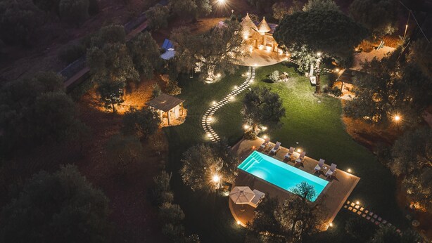 An aerial view of a resort with a swimming pool, lounge chairs, and a well-lit garden area. - Trulli Biancapetra 8 2 Emma Villas (Francavilla Fontana)