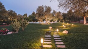 A well-lit garden pathway leading to a pool area with lounge chairs and a pergola. - Trulli Biancapetra 8 2 Emma Villas (Francavilla Fontana)