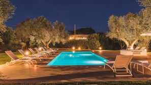 A rectangular swimming pool with lounge chairs and a fire feature, surrounded by trees and a well-lit patio area. - Trulli Biancapetra 8 2 Emma Villas (Francavilla Fontana)