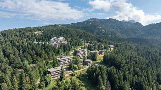 Ein Resort mit mehreren Gebäuden, umgeben von dichtem Wald und Bergen.