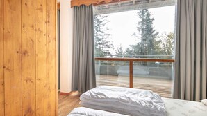 Ein Schlafzimmer mit Holzboden, einem Bett mit weißer Bettwäsche und einem großen Fenster mit Vorhängen.