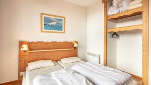 Ein Schlafzimmer mit einem hölzernen Kopfteil, zwei Betten, einem an der Wand montierten Regal, einem gerahmten Bild und einem Holzschrank.