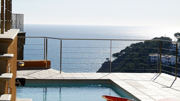 Ein Poolbereich mit Meerblick, eine Liege und ein Gebäude mit Balkon.