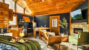 Interior acolhedor de uma cabana com teto de madeira, área de jantar, sala de estar com lareira e cama com vista.