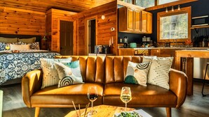 Interior acolhedor de uma cabana, com um sofá de couro, paredes de madeira, uma área de cozinha e uma janela grande.
