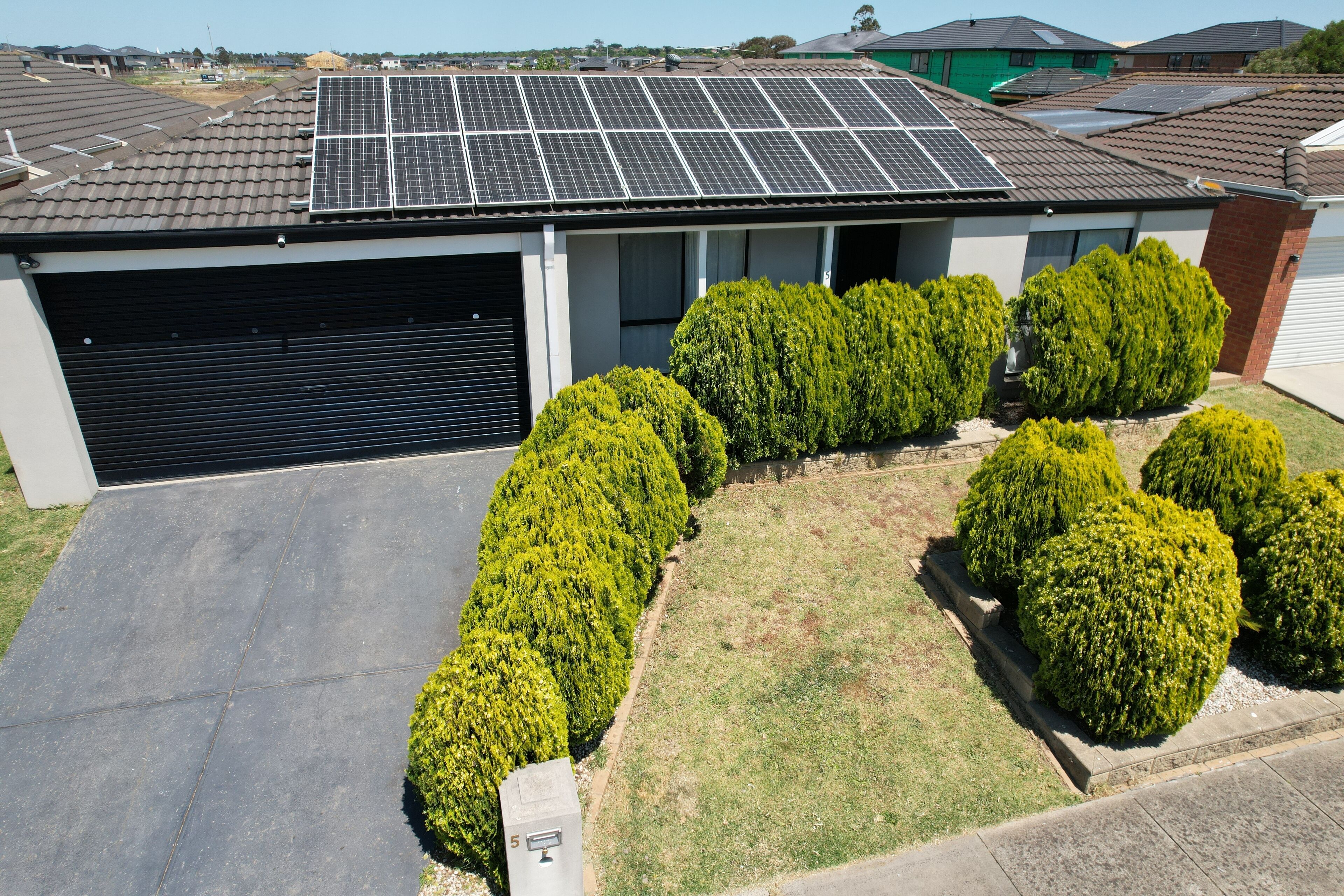 A modern building with a garage, solar panels on the roof, and well-maintained hedges.