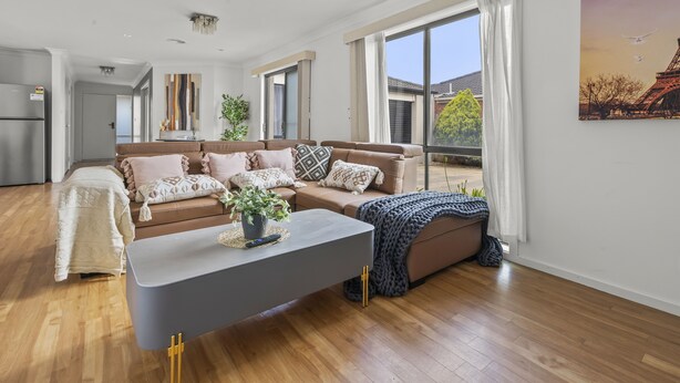 Een moderne woonkamer met een zithoek, een salontafel en een groot raam met gordijnen.