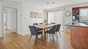 Een moderne keuken met een houten kookeiland, een eethoek met een grote tafel en stoelen, en een aanrecht met wijnglazen.
