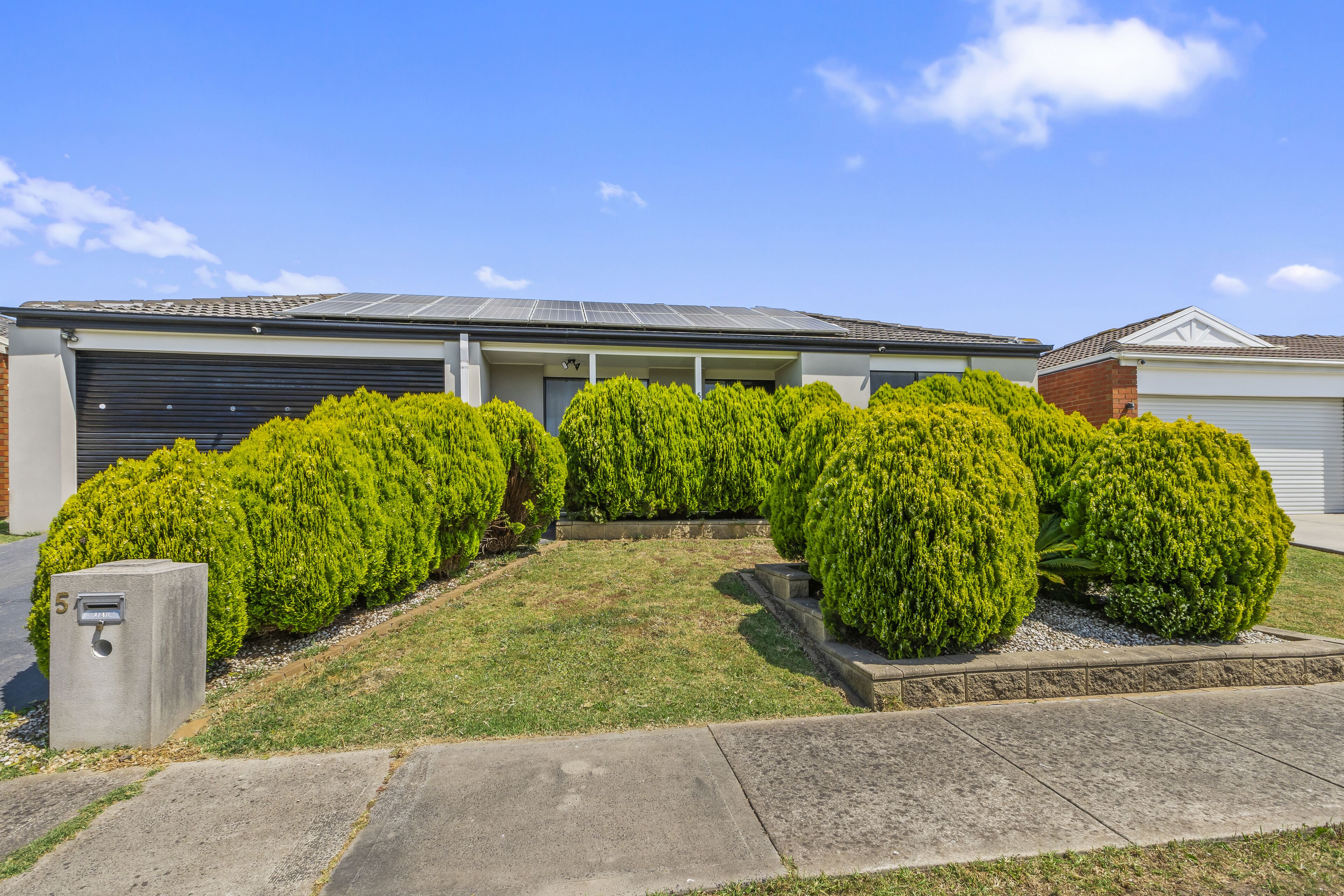 A modern residential building with a garage, solar panels, and well-maintained green lawns and bushes.