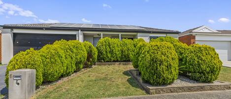 A modern residential building with a garage, solar panels, and well-maintained green lawns and bushes.