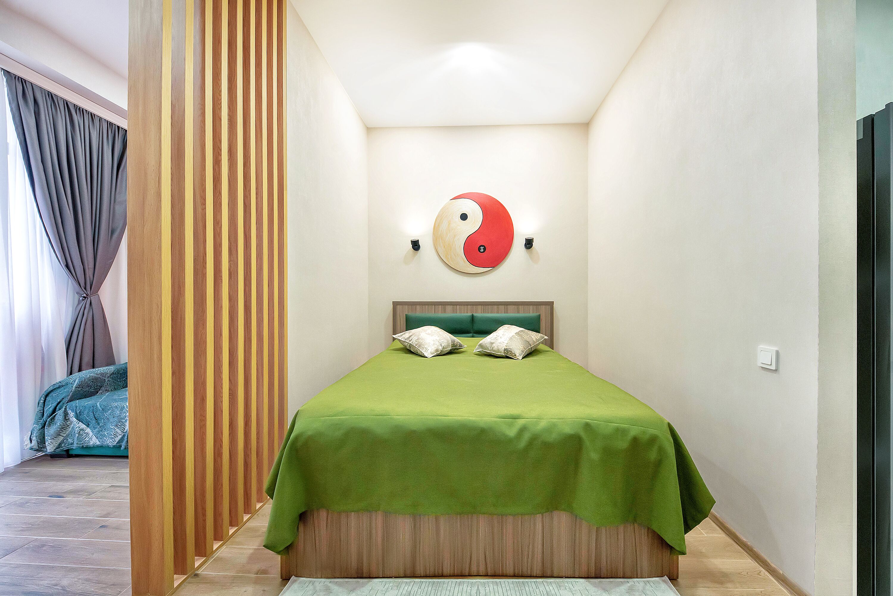 A bedroom with a green bedspread, a wooden headboard, and a yin-yang symbol on the wall.