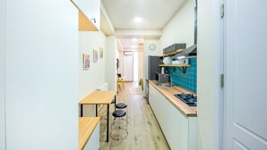 A narrow kitchen with a wooden table and stools, a stove, and a sink. - H&B apartments Akhmeta (Tbilisi)