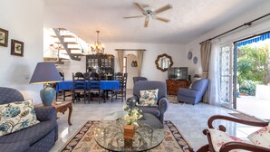 A spacious living room with a glass coffee table, sofas, and a dining area with a blue tablecloth.