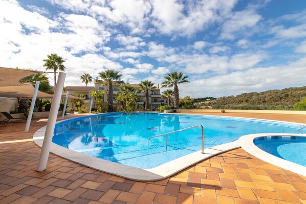 Ein Pool mit gefliestem Deck, Palmen und einem Gebäude im Hintergrund.
