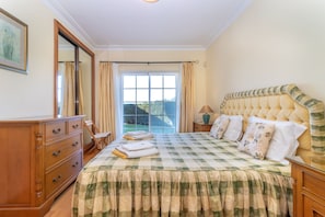 Ein Schlafzimmer mit einem großen Bett, einem Schminktisch, einem Spiegel und einem Fenster mit Vorhängen.