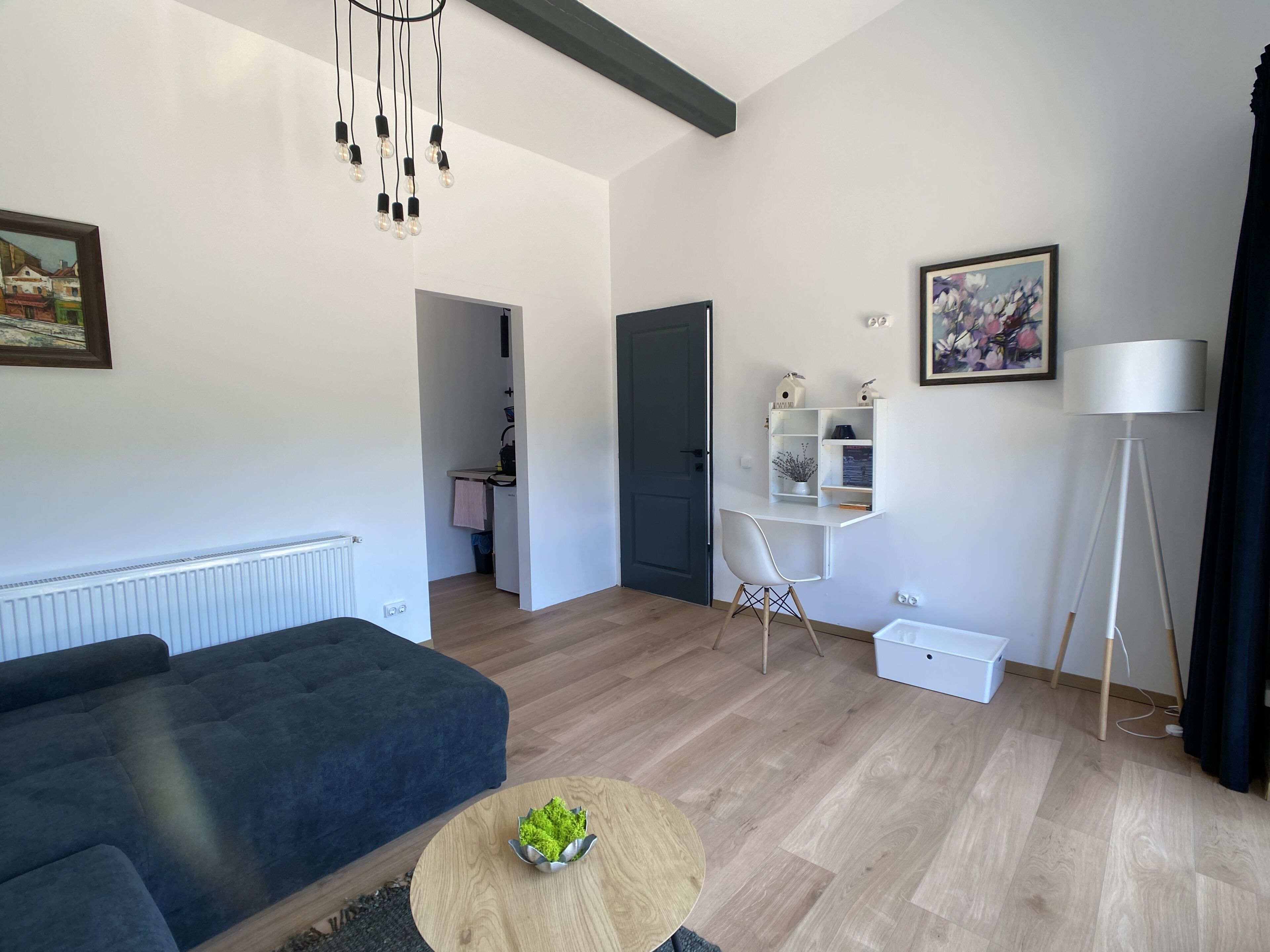 Een moderne woonkamer met een donkere bank, een ronde houten salontafel, een wit bureau met planken, en een vloerlamp.