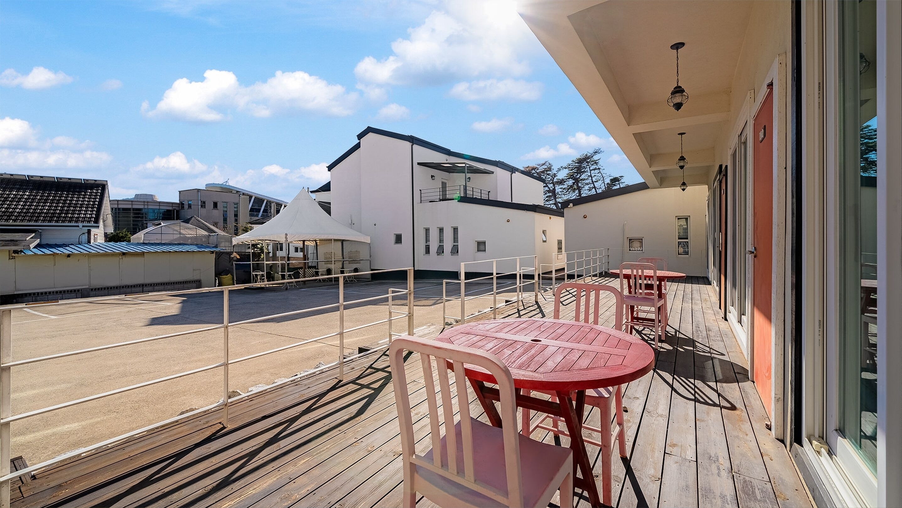 Une terrasse en bois avec une table et des chaises, un espace abrité et un bâtiment en arrière-plan.