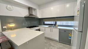 Een moderne keuken met witte kasten, een roestvrijstalen afzuigkap, een inbouwvaatwasser en een klein raam met gordijn.