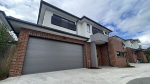 Een modern huis met twee verdiepingen, een grijze garage, een bakstenen gevel en een klein portaaltje.