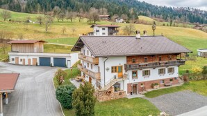 A multi-story building with a sloped roof, a garage, and a balcony. - Cosy holiday apartment near the slopes (Itter)