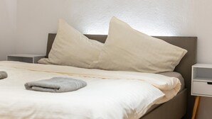 A neatly made bed with pillows and a folded towel, a bedside table, and a nightstand with a lamp. - Cosy holiday apartment near the slopes (Itter)