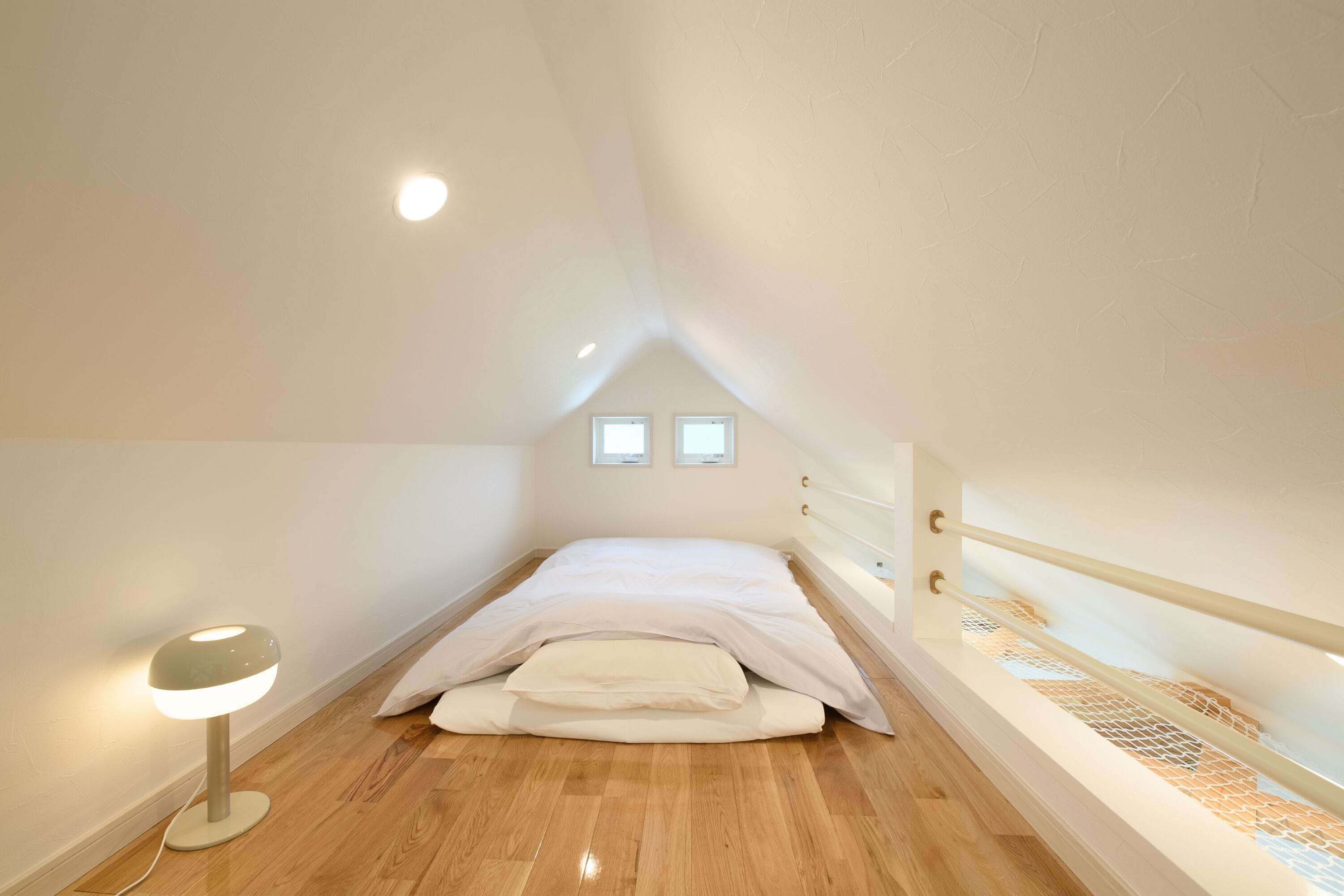 A small, triangular attic bedroom with a bed, a bedside lamp, and a window.