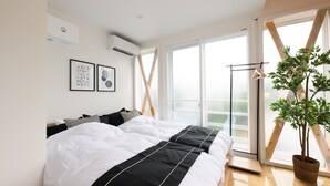 Une chambre avec un grand lit, une plante en pot et une vue sur l’extérieur grâce à une grande fenêtre.