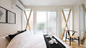 A modern hotel room with a large bed, a chair, and a view through a glass door.