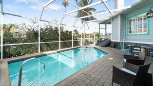 Une piscine intérieure à l’eau d’un bleu cristallin, entourée d’une structure en verre, et aménagée avec des fauteuils et une table en osier.
