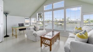 Un salon spacieux avec un plafond haut, de grandes fenêtres et une vue sur un port de plaisance.