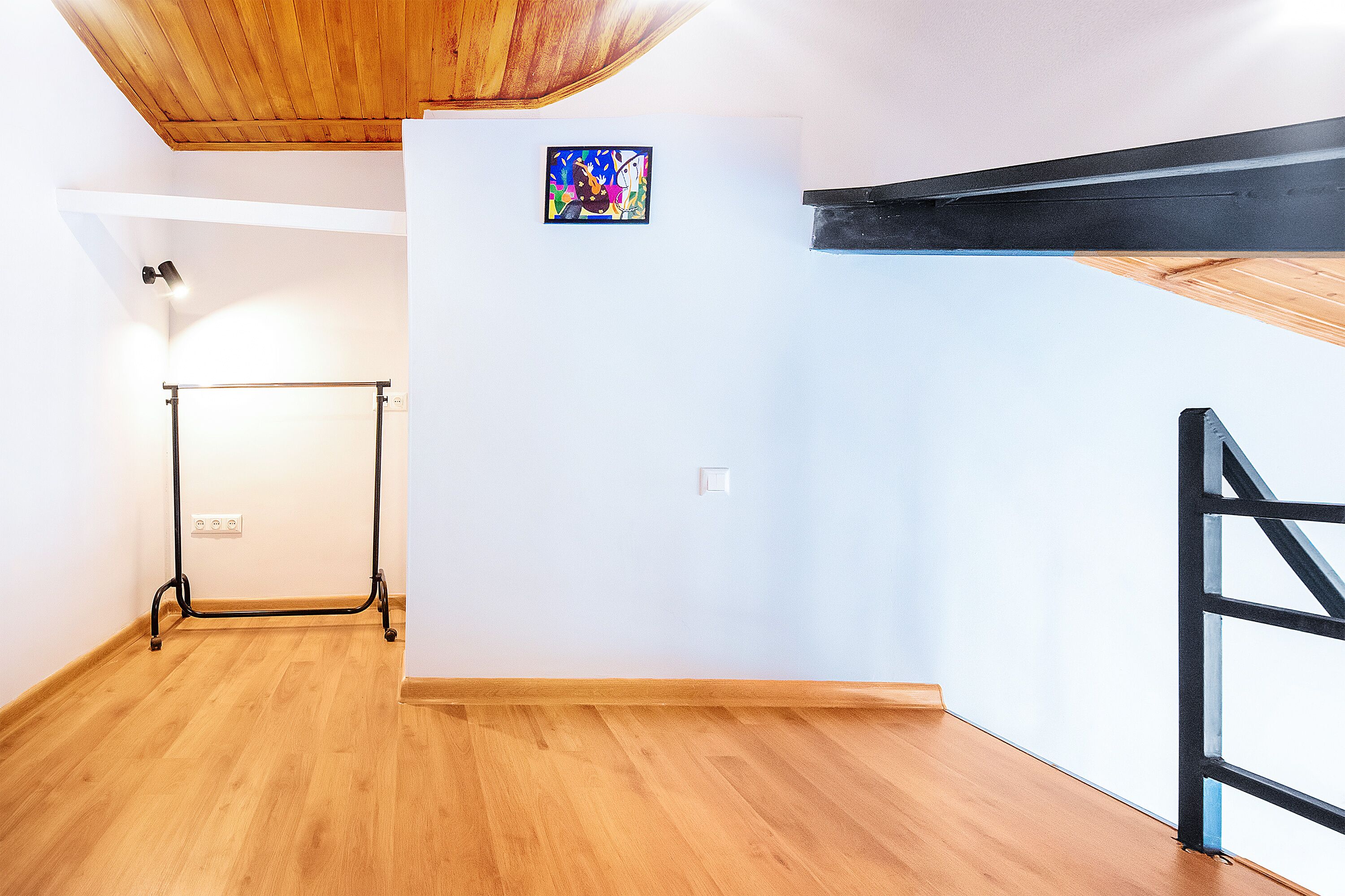 A room with wooden flooring, a black metal frame structure, and a small colorful artwork on the wall.