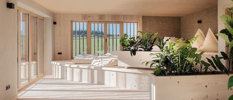 Un interior moderno con suelo de madera, un conjunto de sofás y un amplio ventanal con vistas a la vegetación.