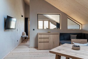 A modern interior with a wooden floor, a TV mounted on the wall, a sofa, a table with a bowl, and a cabinet. - Ferienwohnung 1, 48qm (Eggstätt)