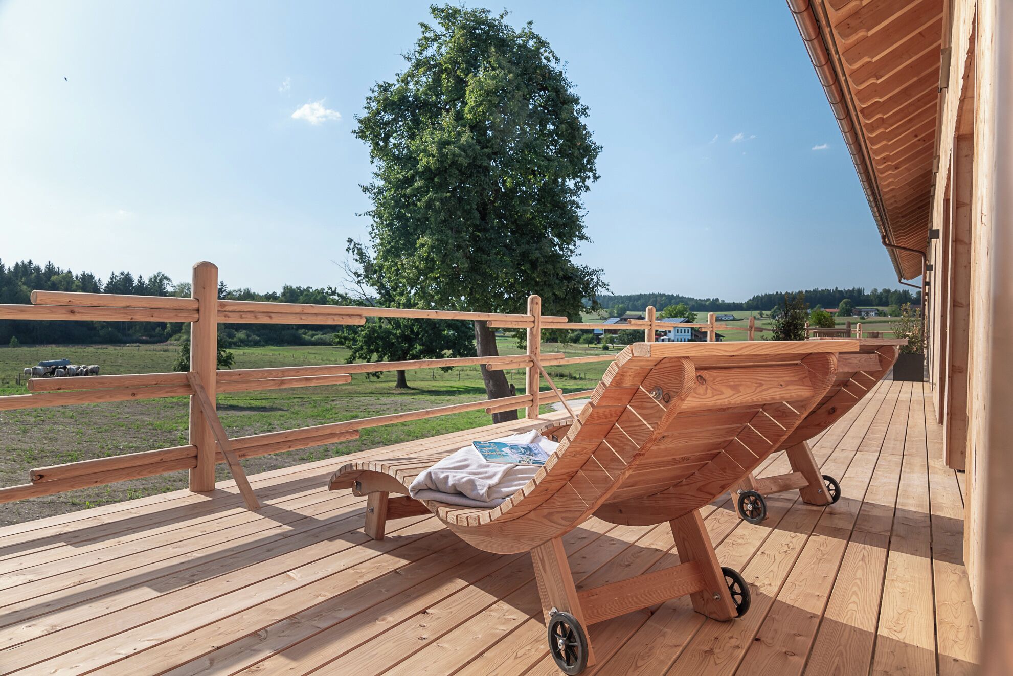 Une terrasse en bois avec un fauteuil de relaxation et une vue sur un arbre et le paysage.