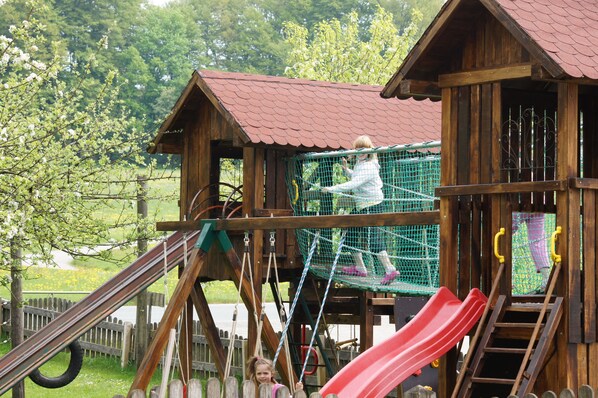 Kids can climb, slide, and play on this outdoor structure with a rustic design and red roof.
