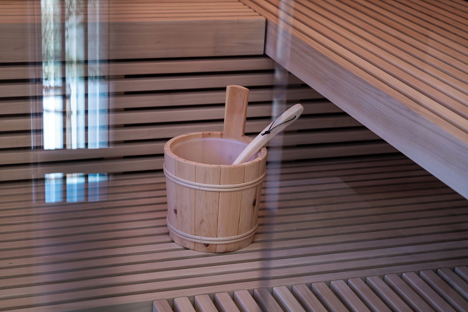 Un seau en bois contenant une cuillère, posé sur un plancher en bois à lattes.