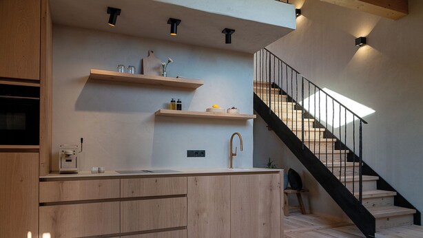 A modern kitchen with wooden cabinetry, a built-in sink, and a black staircase with a railing. - Ferienwohnung 2, 48qm (Eggstätt)